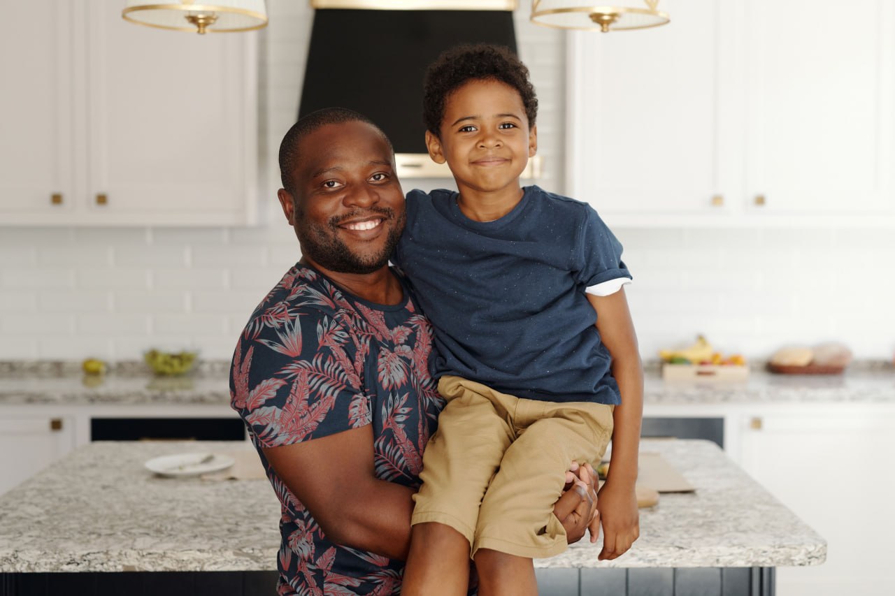 A smiling father holding his young son in a bright kitchen
